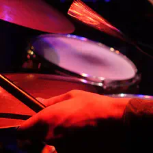 A close-up shot of a person's hand holding drumsticks over a drum set. The scene is illuminated with red and purple stage lights, creating a vibrant and dynamic atmosphere
https://www.flickr.com/photos/ztec/53891143917/