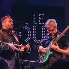 Concert photography of Kyle Eastwood playing Electric bass. he is looking at his hands and cords. Wear glasses. 
Also, there is Quentin Collins waiting to start playing Trompette eyes closed.
https://www.flickr.com/photos/ztec/53408157245/
Albums: www