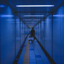 A man is pulling a chariot with a big case on it in the metro corridor.