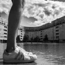 Deux pieds sur l'eau, un peu flou devant un bâtiment d'habitation moderne en U avec quelques nuages dans le ciel