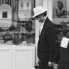 A man walking looking down. He has a white hat.