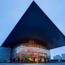 Picture of the Copenhagen opera. A bubble with glowing orange from inside (actually wood) right below a flat square that act as a roof, but go way longer outside the bubble. The picture is deforming the square making one corner pointing to the top border of the picture. Main colors are blue shared everywhere, except the bubble interior.  
https://www.flickr.com/photos/ztec/53132985520/