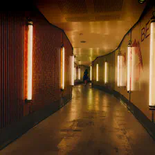 A corridor with neon lights on each walls (vertical). The corridor is zigzaging. We can see a woman walking in the end.