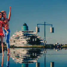 Two dolls on water with a giant (real) cruise boat in the back.