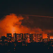 Paris from afar with the Eiffel tower. Clouds of smoke lighted in orange is visible behind buildings and the tower.